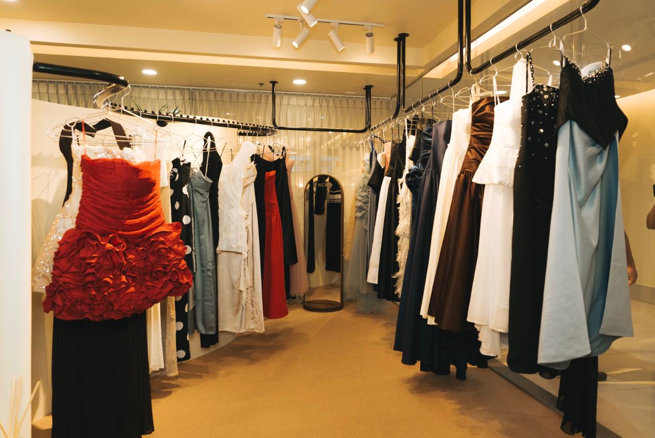 Interior of a formal dress boutique with racks of gowns along both sides and a red ruffled dress in the foreground.