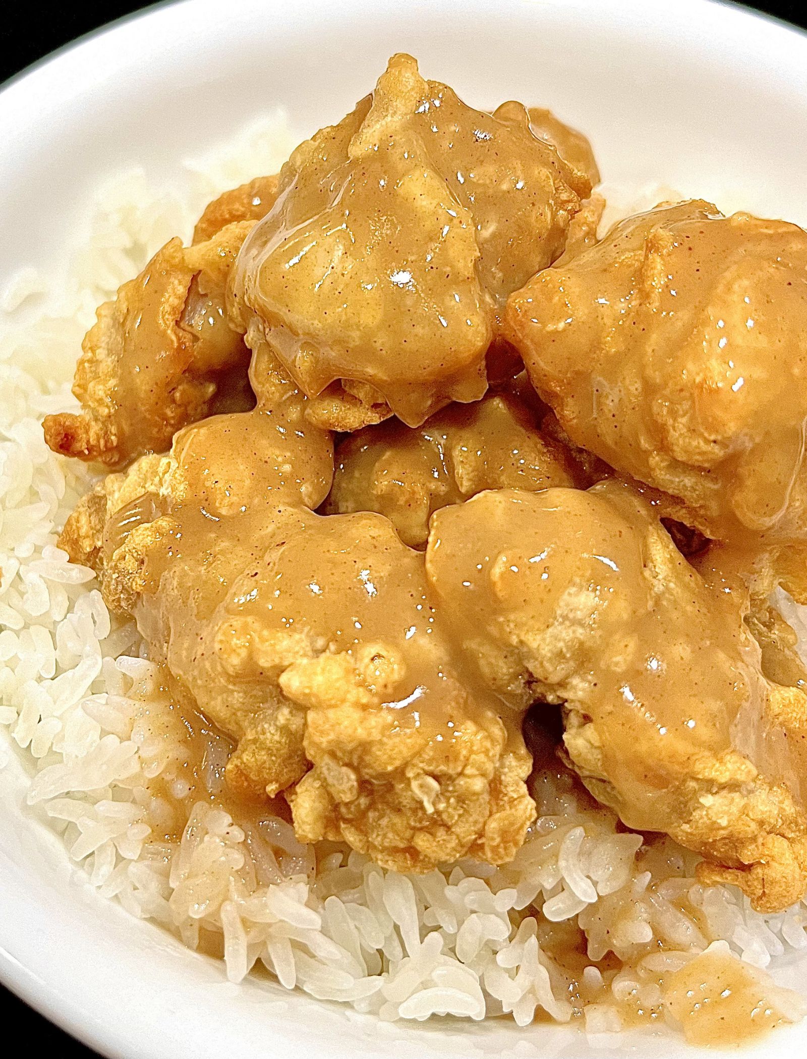Fried chicken pieces covered in creamy brown sauce served over steamed white rice in a bowl