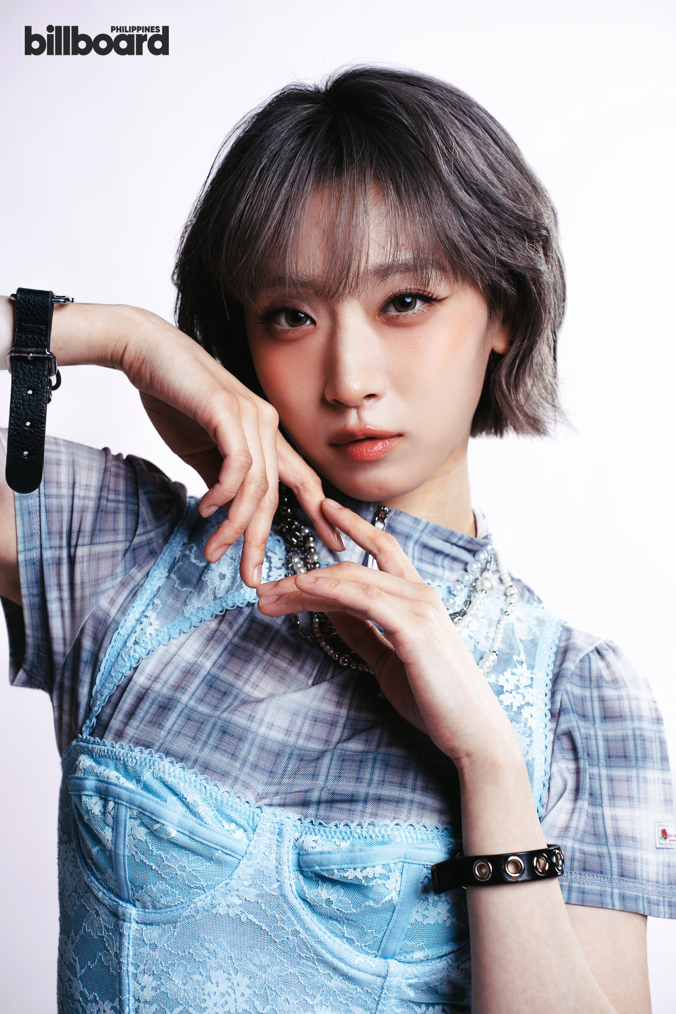 Portrait of a young woman wearing a blue lace dress, posing with her hands near her face with a billboard Philippines logo in the corner.