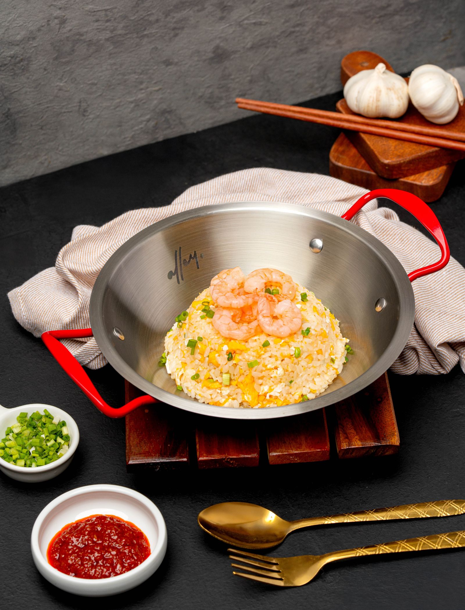 Shrimp fried rice in a stainless steel pan with red handles, garnished with chopped green onions.