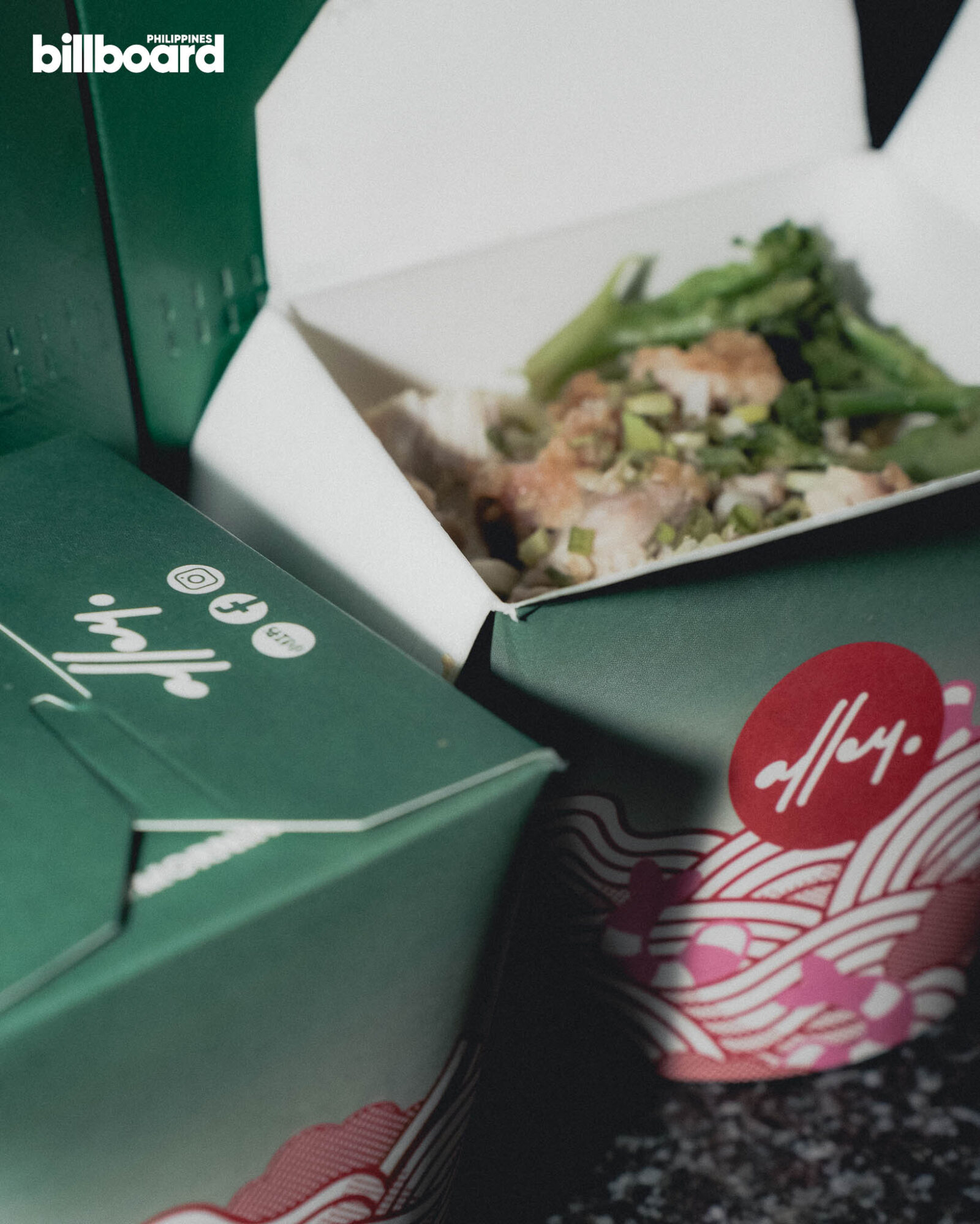 Open takeout box of a meal with chopped greens inside, surrounded by green packaging boxes with the Billboard Philippines logo in the corner.