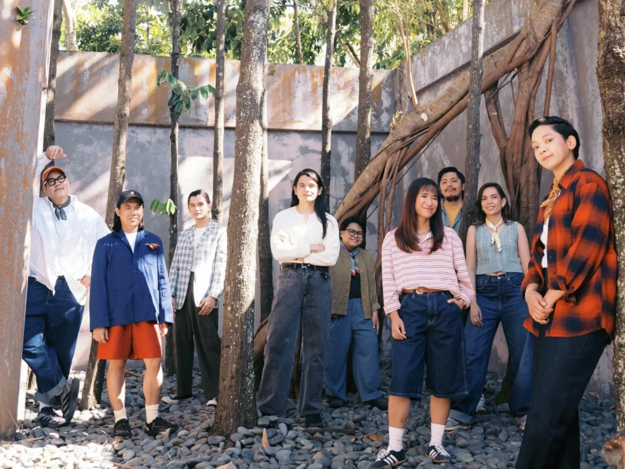 Group of diverse young adults posing outdoors among trees, smiling at the camera.
