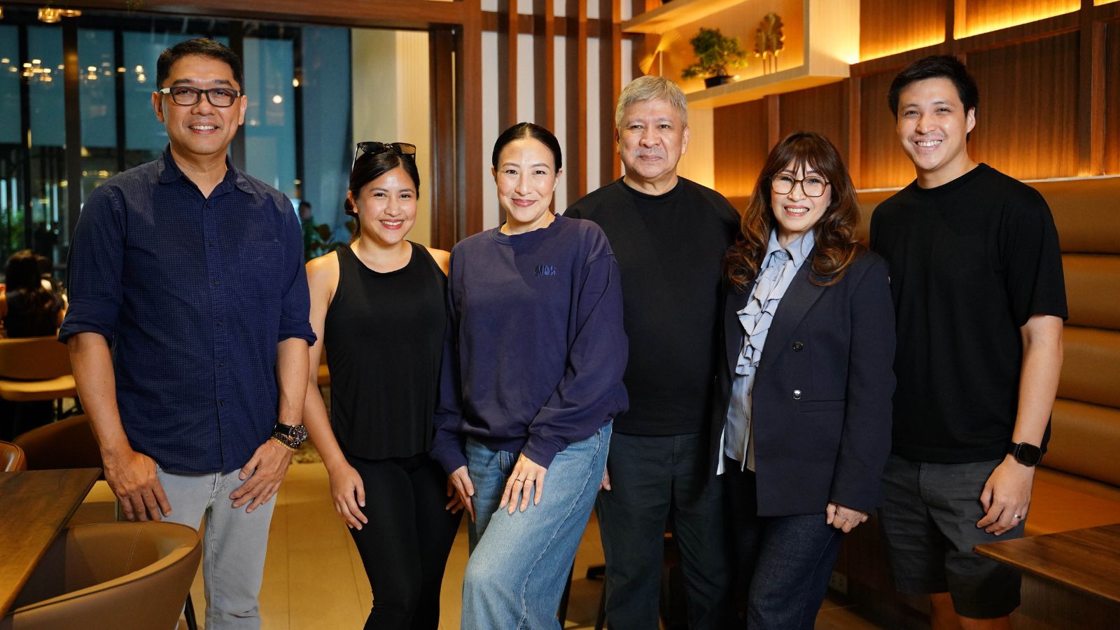 Six people posing together in a warmly lit restaurant, smiling at the camera.