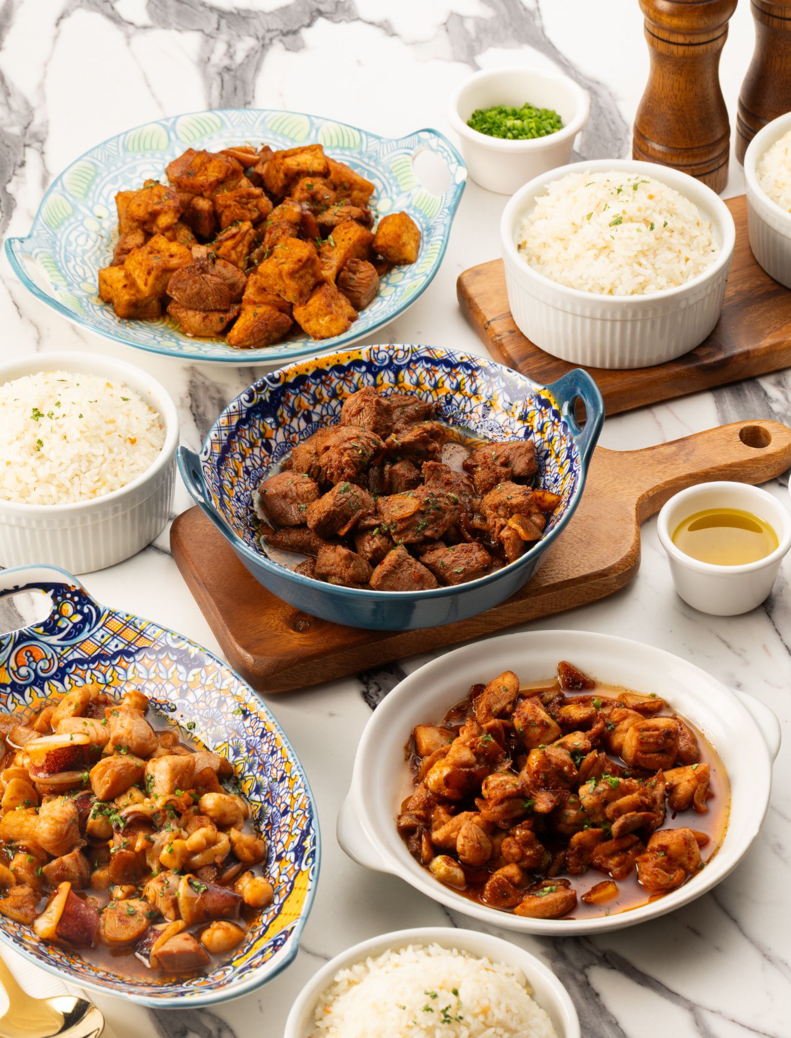 Assorted Asian dishes on a marble surface: bowls of white rice and braised meats in colorful ceramic bowls.