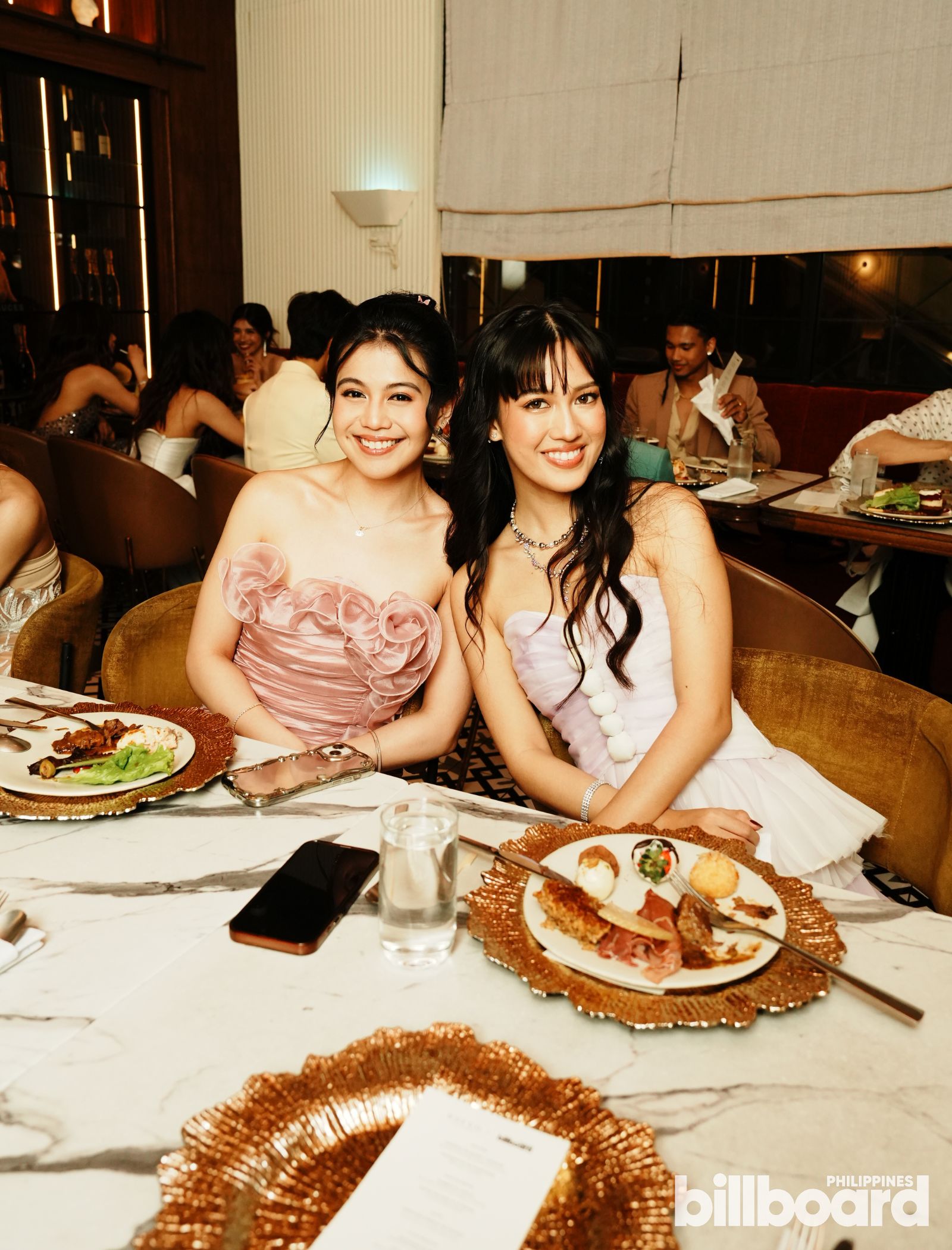 Two young women in pastel formal dresses dining at Bueno Tapas & Wine Restaurant during the Billboard Philippines Women In Music 2026 dinner.