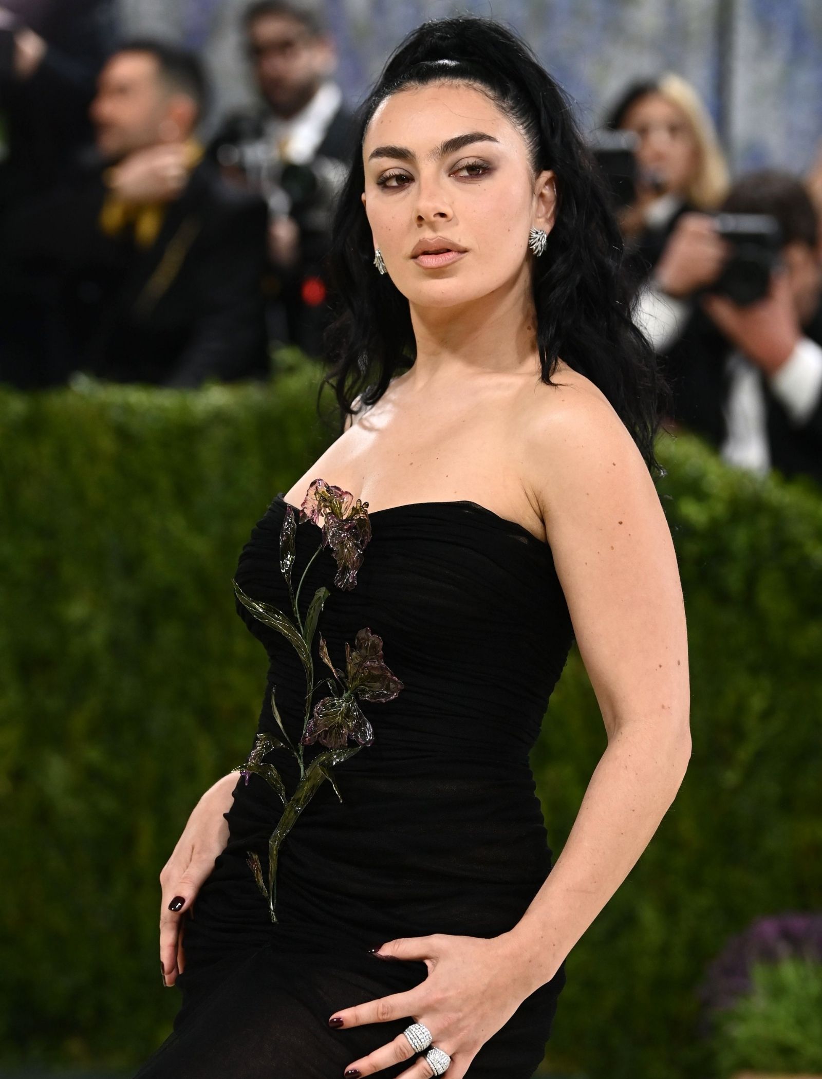 Woman with dark hair in an off-shoulder black gown featuring floral embellishments, posing for photographers.