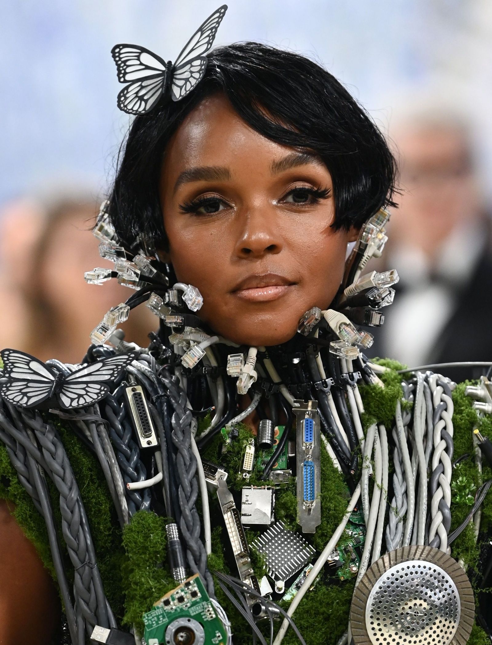 Model wearing an avant-garde outfit built from discarded electronics, with a butterfly hair accessory.