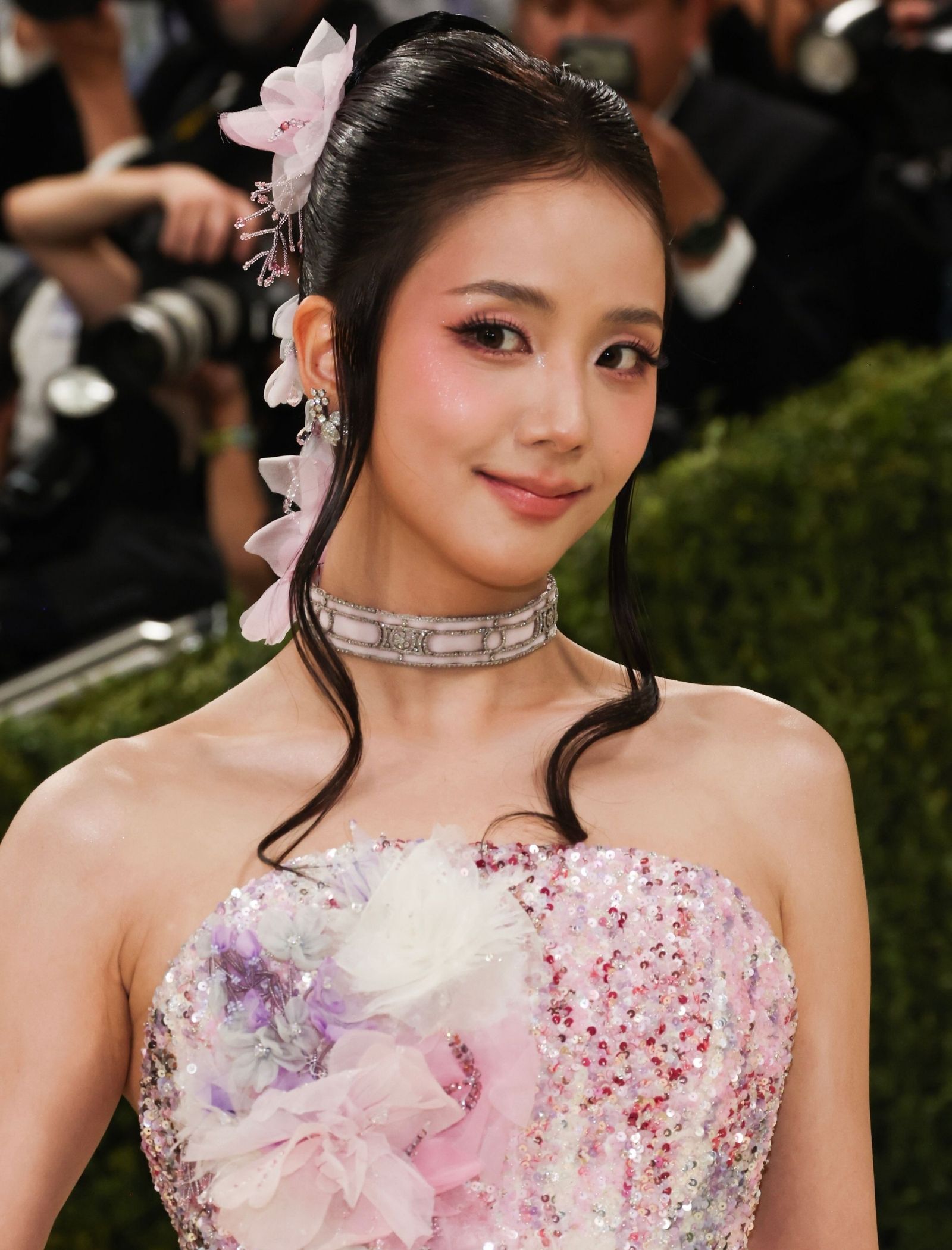 Close-up of a smiling woman in a pink sequined gown with a pink flower hairpiece at a formal event.