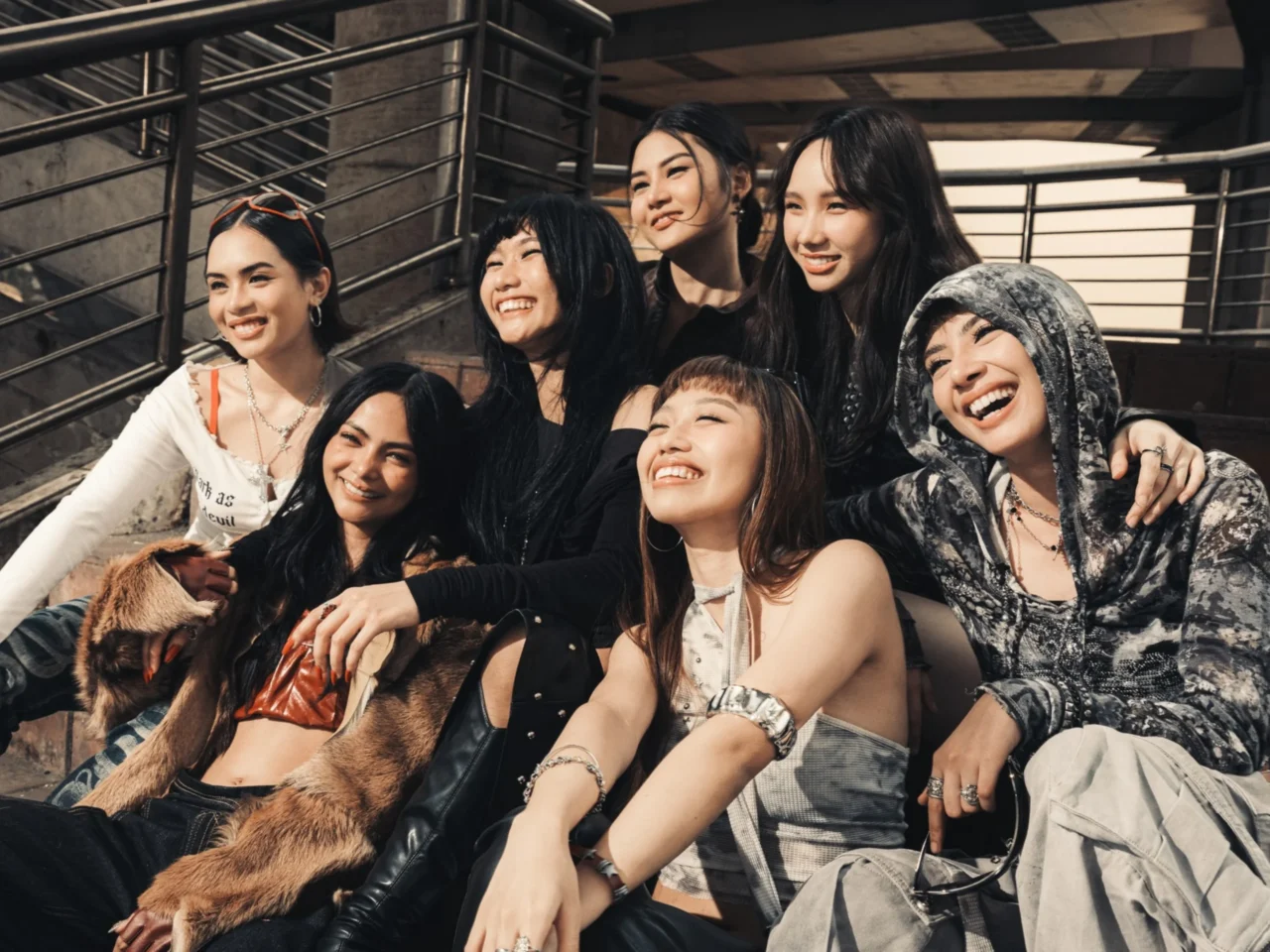 A group of eight friends posing together on stairs, smiling and having fun in casual trendy outfits.