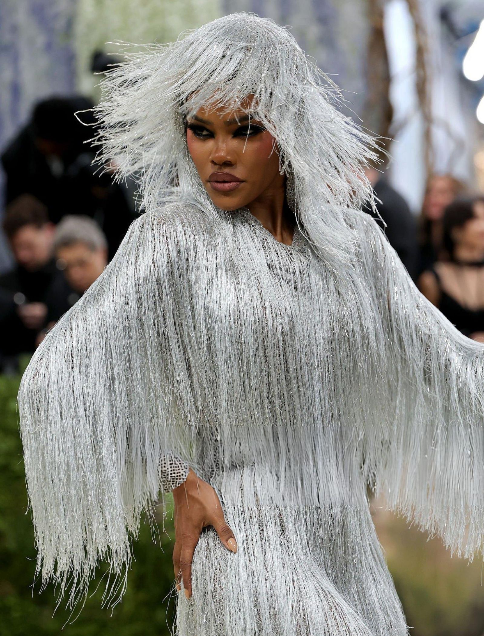 Person wearing a shimmering silver fringe outfit with a dramatic fringe hood, outdoors in a fashion setting.