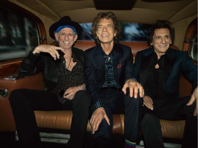 Keith Richards, Mick Jagger, and Ronnie Wood of the Rolling Stones seated in the back of a car smiling