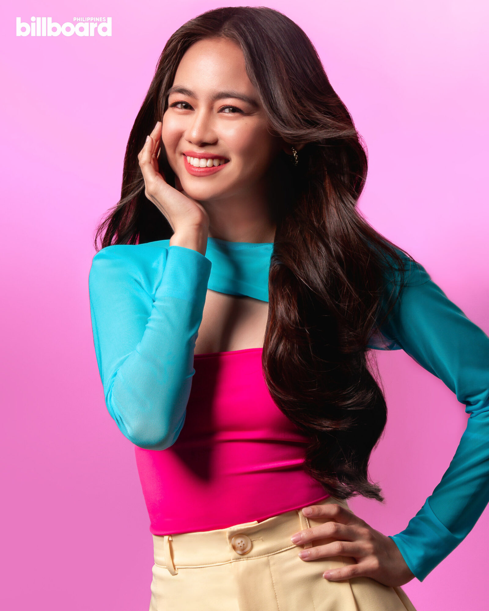 Ashtine Olviga dressed in vibrant clothes posing in front of pink background