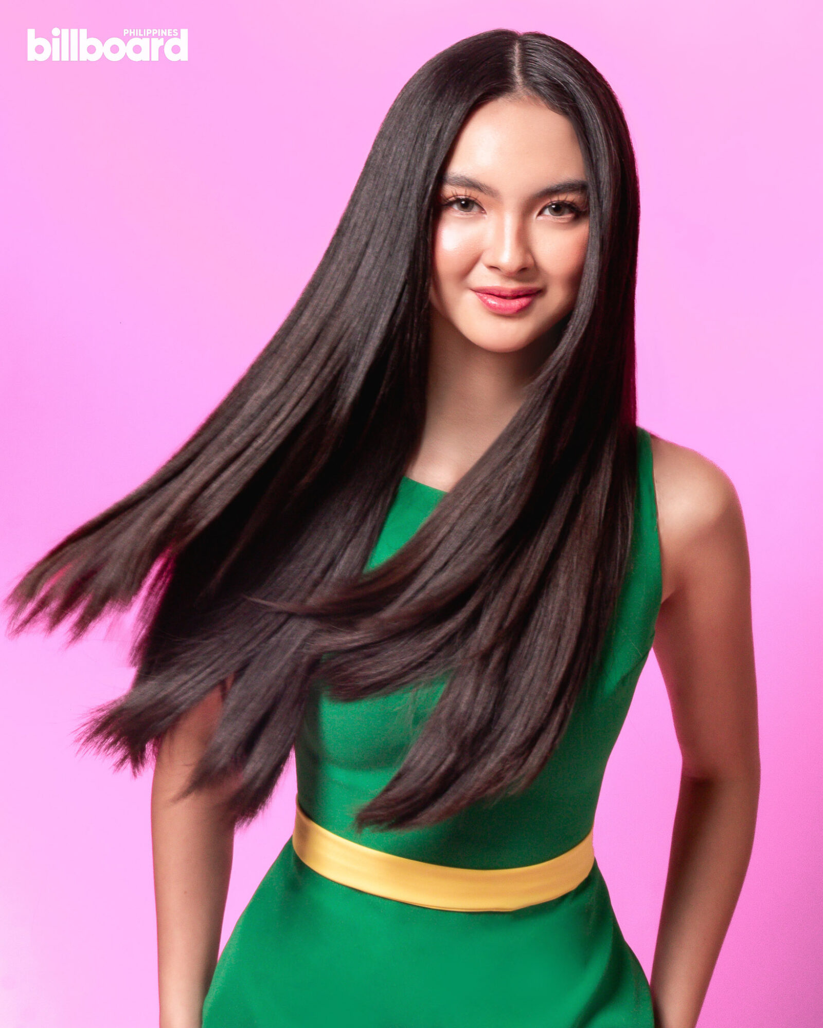 Kai Montinola in a green dress posing in front of a pink background